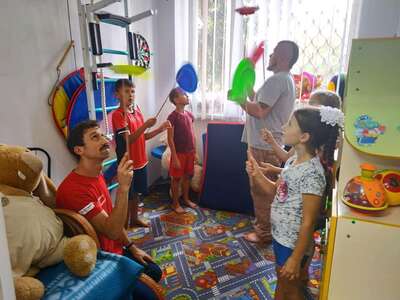 Children are practising circus show tricks (spinning plates) in a colourful room.