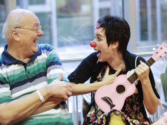 old man laughing with female clown holding guitar 